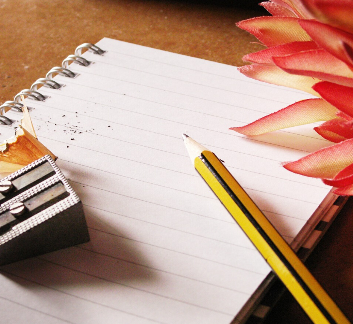 Photo of a notepad, a pencil, and a flower