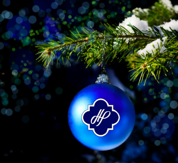Blue ornament with town logo hanging on a snow capped pine branch