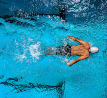 above view of a man swimming in a pool lane, wearing a white swim cap and dark shorts