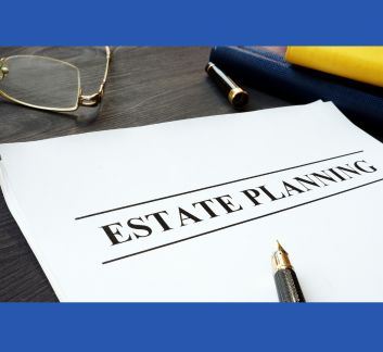 The words estate planning on a sheet of paper on a desk with a pen and a pair of eyeglasses.