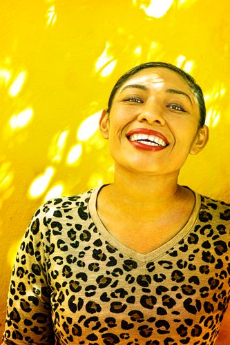 Photograph of a smiling woman in a cheetah print shirt and a yellow background.