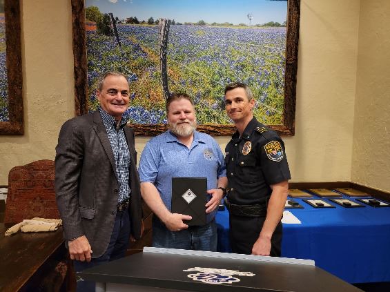 Three men standing together smiling at camera, the center man holds a certificate.